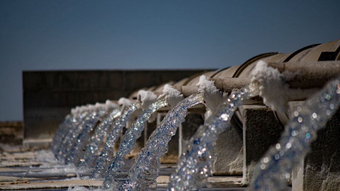 Close-up view of water flowing from industrial pipes against a clear blue sky.