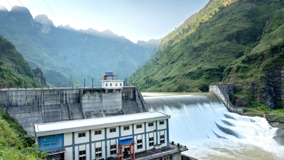 A hydroelectric dam surrounded by lush green mountains under a clear blue sky.