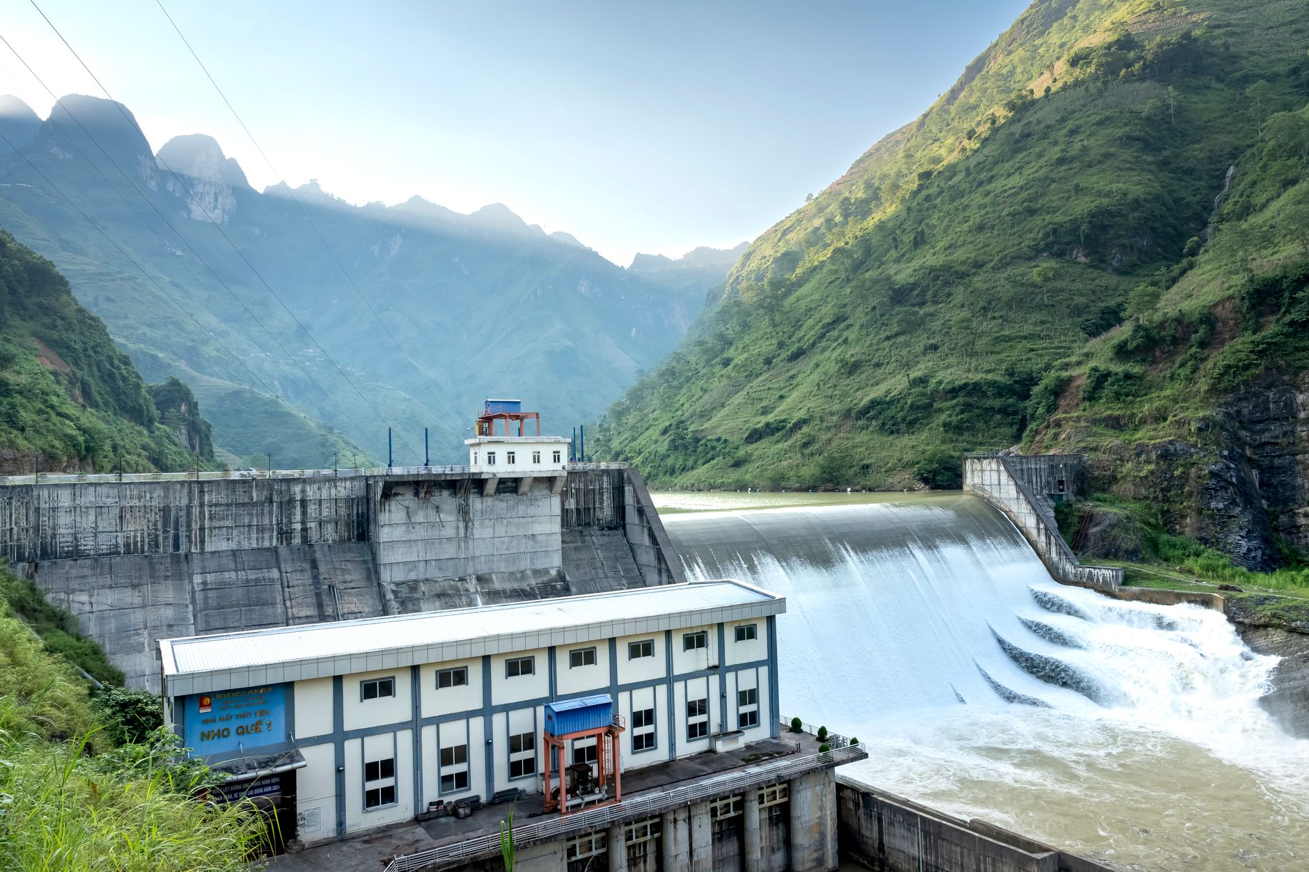 A hydroelectric dam surrounded by lush green mountains under a clear blue sky.
