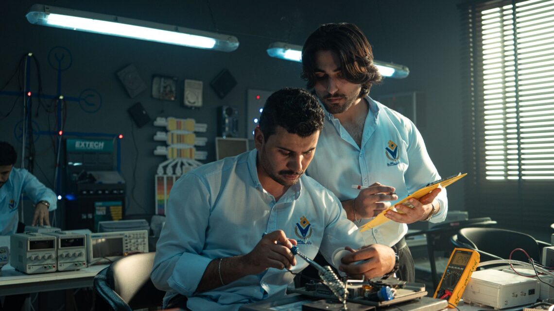 Two men working on an electronics project in a Baghdad lab, focused and collaborating.