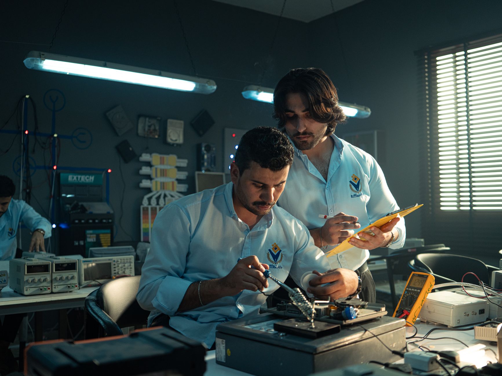 Two men working on an electronics project in a Baghdad lab, focused and collaborating.