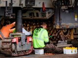 Engineers performing maintenance on construction equipment in an industrial workshop setting.
