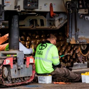 Engineers performing maintenance on construction equipment in an industrial workshop setting.